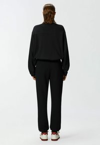 Zwarte oversized sweatshirt met een naden detail, gecombineerd met tapered zwarte broeken. Outfit compleet met witte en rode sneakers.