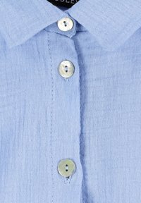 Light blue linen shirt with a collared neckline, featuring four round buttons made of a shiny, reflective material. Textured fabric.