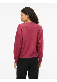 Pull en maille polaire de couleur baies profondes, avec un col rond, des épaules tombantes et un ourlet côtelé. Texture douce, coupe décontractée.