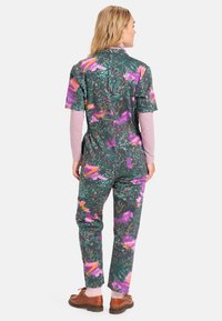 Blomstertrykt jumpsuit i mørkegrønn, med livlige rosa, lilla og oransje tropiske mønstre, korte ermer og avslappet passform.
