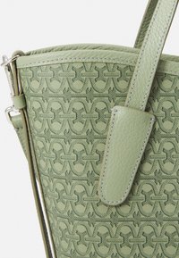 Green textured handbag with embossed pattern, featuring a smooth leather strap and subtle stitching details, showcasing a structured design.