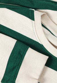 Tissu rayé vert et crème, avec un col et des poignets côtelés, texture douce et design décontracté.
