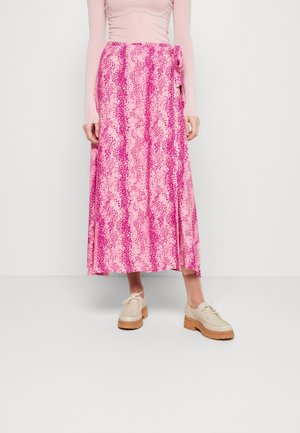 Jupe maxi rose avec un motif en serpent, dotée d'un détail de nouage sur le côté et d'un tissu léger. Associée à des chaussures beiges à lacets.