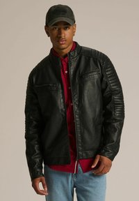 Czarna skórzana kurtka motocyklowa z żebrowanymi detalami na ramionach i kieszeniami na zamek, noszona na czerwonej koszuli, w zestawieniu z jasnoniebieskimi dżinsami.