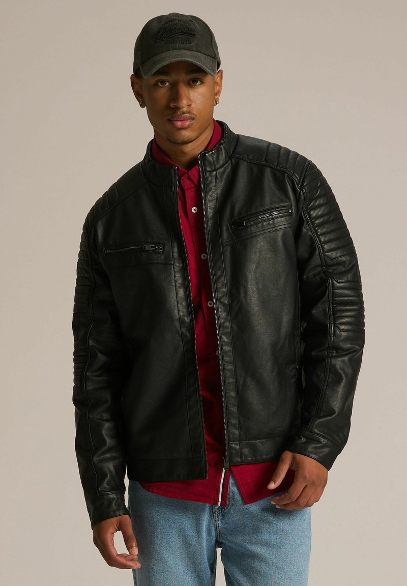 Czarna skórzana kurtka motocyklowa z żebrowanymi detalami na ramionach i kieszeniami na zamek, noszona na czerwonej koszuli, w zestawieniu z jasnoniebieskimi dżinsami.