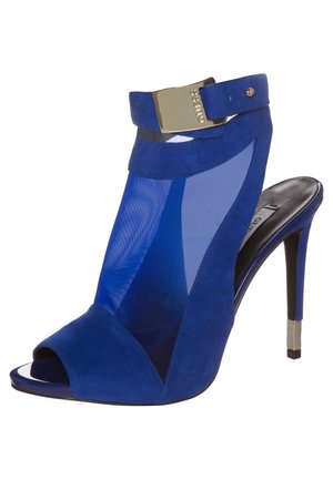 Blå suedestiletter med meshpanel, åben tå, spændeaccent ved anklen og en metallisk kvadratisk hældetalje.