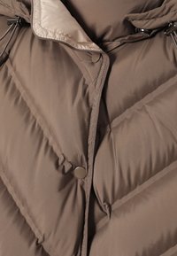 Veste matelassée marron avec boutons-pression et capuche ajustée dotée de cordons de serrage réglables et doublure intérieure beige.