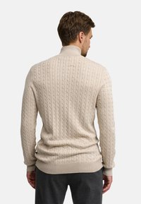 Beżowy sweter z dzianiny z teksturowanym splotem w kabli, z prążkowanymi mankietami i hemem. Wysoki kołnierz; miękka tkanina o dopasowanym fasonie.