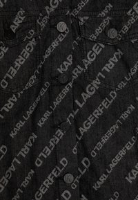 Zwarte denimstof met een herhalend grijs "KARL LAGERFELD" logo patroon. Zwarte metalen knopen met reliëf 'K' accenten.