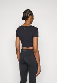 Čierne krátke tričko s krátkymi rukávmi, s okrúhlym výstrihom a drobným logom. Kombinované s čiernymi legínami s vysokým pásom.