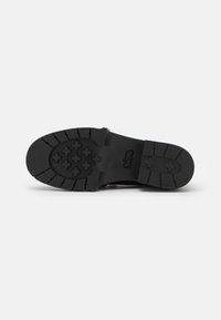 Black rubber shoe sole with a tread pattern featuring rounded and cross shapes. Smooth texture with raised grip details for traction.