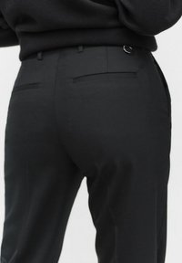 Zwarte broek met een gladde textuur, voorzien van een aansluitende silhouet, achterzakken en een metalen lus accent nabij de tailleband.