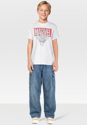 Hvid bomulds T-shirt med rød "MARVEL" grafik og edderkopillustration, kombineret med blå denim cargo-bukser og gule sneakers.