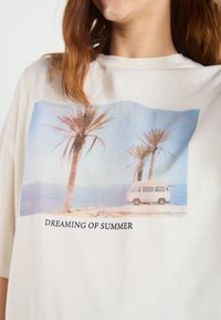 Cream-colored oversized t-shirt with a printed graphic of palm trees and a van, featuring the text "DREAMING OF SUMMER" below.