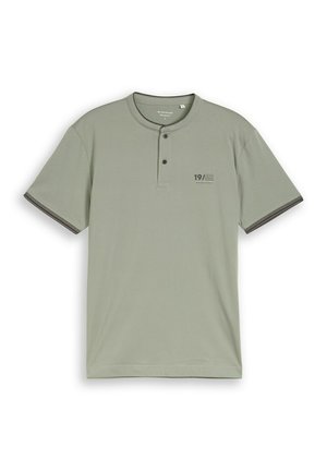 Tricou Henley cu mâneci scurte, verde deschis, cu doi nasturi închiși, margini închise la manșete și inscripția "19/62" pe piept.