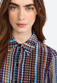 Camicia multicolore con colletto, caratterizzata da strisce verticali e un motivo a pied-de-poule in colori vivaci. Tessuto morbido con dettagli a bottoni.