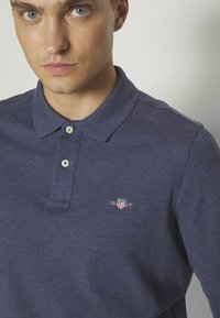 Navyblaue Polo-Shirt aus strukturiertem Stoff, mit einem 2-Knopf-Kragen und kleinem gesticktem Logo auf der linken Brust.