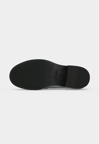Semelle de chaussure noire avec grip texturé, nom de marque embossé « ANNARFELD » et taille « 37 » visible sur un fond clair uni.