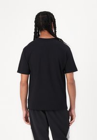T-shirt noir à manches courtes, design col ras du cou, texture douce, coupe décontractée, avec des coutures visibles sur l'arrière des épaules.