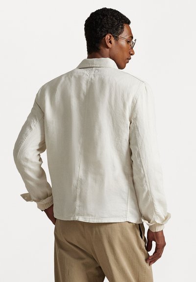 Cream-colored jacket with a relaxed fit, structured collar, and ribbed cuffs. Textured fabric, minimal seams, and a straight hem.