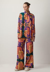 Színes, mintás öltözet, amely hosszú ujjú gombos inget és bő szárú nadrágot tartalmaz. Az anyag virágos és geometrikus mintákkal van díszítve, élénk színekben.