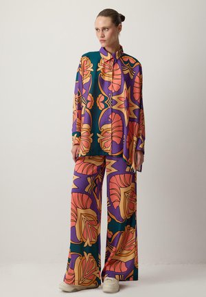 Šarena, šarena odjeća koja se sastoji od košulje dugih rukava s gumbima i hlača širokih nogavica. Tkanina sadrži cvjetne i geometrijske uzorke u živopisnim nijansama.