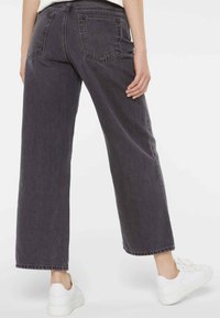 Dark gray wide-leg jeans with a high waist, featuring two back pockets and raw edges, paired with white sneakers.