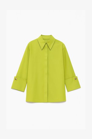 Koszula w kolorze chartreuse z długim rękawem, szerokimi mankietami i guzikami, ukrytymi guzikami z przodu oraz spiczastym kołnierzykiem, ułożona na płasko na białym tle.