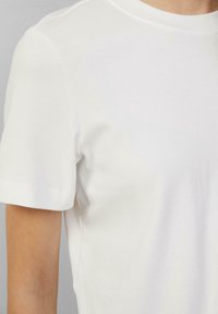 Biała bawełniana koszulka z okrągłym dekoltem i krótkimi rękawami. Gładka faktura, minimalne szwy i brak widocznych nadruków lub ozdób.