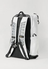 Zaino bianco con accenti neri, dotato di spallacci imbottiti, accessori in plastica e un motivo triangolare unico sul retro. Chiusura con zip e tasche laterali.