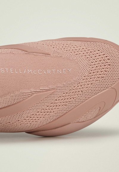 Zapatilla de color rosa claro con parte superior tejida, detalles lisos y suela de goma resistente. Marca visible en texto blanco a lo largo del lateral.