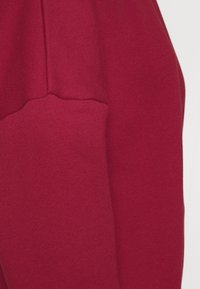 Manga de sudadera roja con una textura suave y lisa. Presenta un puño acanalado y una costura en el hombro, exhibiendo un color sólido sin patrones.