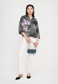 Camicia di raso nera con stampa floreale, vestibilità ampia e maniche corte. Abbinata a pantaloni bianchi a gamba larga e una piccola borsa in denim blu.