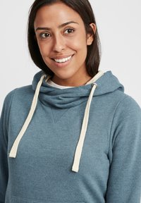 Sudadera con capucha de suave tela azul, con cordones crema, bolsillo tipo canguro y un detalle de costura triangular en el cuello.