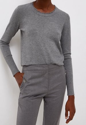 Person wearing a fitted grey long-sleeve sweater with ribbed cuffs and collar, paired with matching grey tailored pants with side pockets.