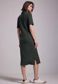 Abito midi verde a costine con colletto, maniche corte e spacchi laterali. Abbinato a sneakers bianche con dettagli verdi sul tallone.