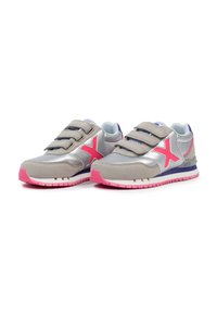 Zapatillas deportivas grises con acentos plateados, suela rosa y un logo X rosa; cuentan con tres correas de gancho y bucle y una parte superior texturizada.