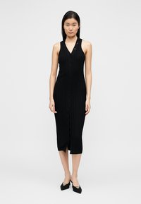 Robe en maille côtelée noire avec encolure en V, design sans manches, fermeture à boutons sur le devant et longueur mi-cuisse. Présente des détails texturés subtils.