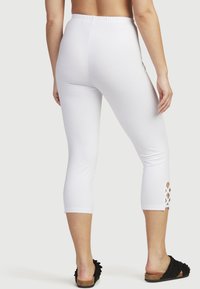 Vita capri leggings i stretchtyg. Har ett elastiskt midjeband och en skärning på nederbenet. Bärs med svarta slip-on skor.