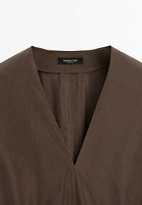 Brown garment with a V-neckline and a black Massimo Dutti label sewn inside the collar.