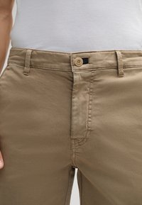 Pantalones caqui con una textura suave, que cuentan con un cierre frontal de cremallera y bot�ón, detalles cosidos y una pequeña etiqueta de tela oscura.