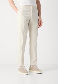 Crème-kleurige, gestructureerde broeken met een rechte pasvorm en zijzakken, gecombineerd met lichtbeige sneakers en een wit shirt.