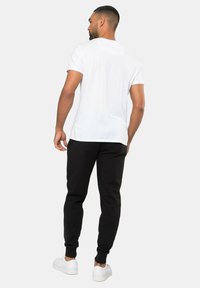 Witte katoenen T-shirt gecombineerd met zwarte joggingsbroek en witte sneakers. Eenvoudig ontwerp met korte mouwen en een relaxed fit.