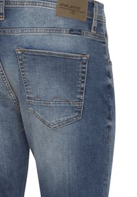 Vaqueros de mezclilla en azul claro con un acabado desgastado, que presentan un bolsillo trasero con una costura en zigzag de contraste y una etiqueta marrón en la cintura.