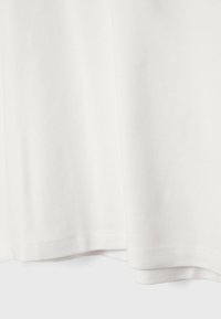 T-shirt bianco in cotone con una superficie liscia, dotato di colletto rotondo e orlo dritto. Il tessuto cade morbido, con dettagli di cucitura ben rifiniti.