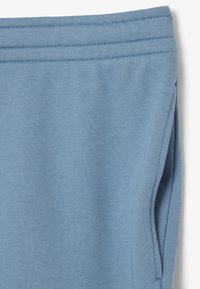 Pantalones deportivos de color azul claro con textura suave, cintura elástica y bolsillos laterales. El material parece suave y cómodo.