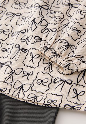 Flødefarvet stof med en struktureret overflade med en sort sløjfe og en scallop-mønster, suppleret med en mørk ribbet kant.