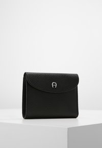 Portafoglio in pelle nera con superficie testurizzata, patta arrotondata e logo argento sul davanti. Design compatto con un'estetica pulita e minimalista.