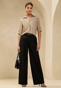 Blusa beige con un cuello, pantalones de pierna ancha negros y un bolso negro. Los tacones de aguja y un cinturón negro completan el conjunto.