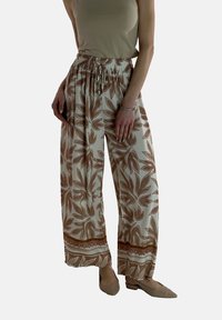 Lichte, wijde broekspijpen in roomkleur met een bruine bloemenpatroon, voorzien van een smocktailband en een contrasterende decoratieve rand aan de zoom.